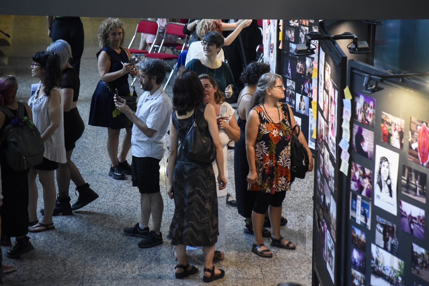 A crowd of visitors moving along tall black panels densely covered with photographs of feminist protests and public actions.