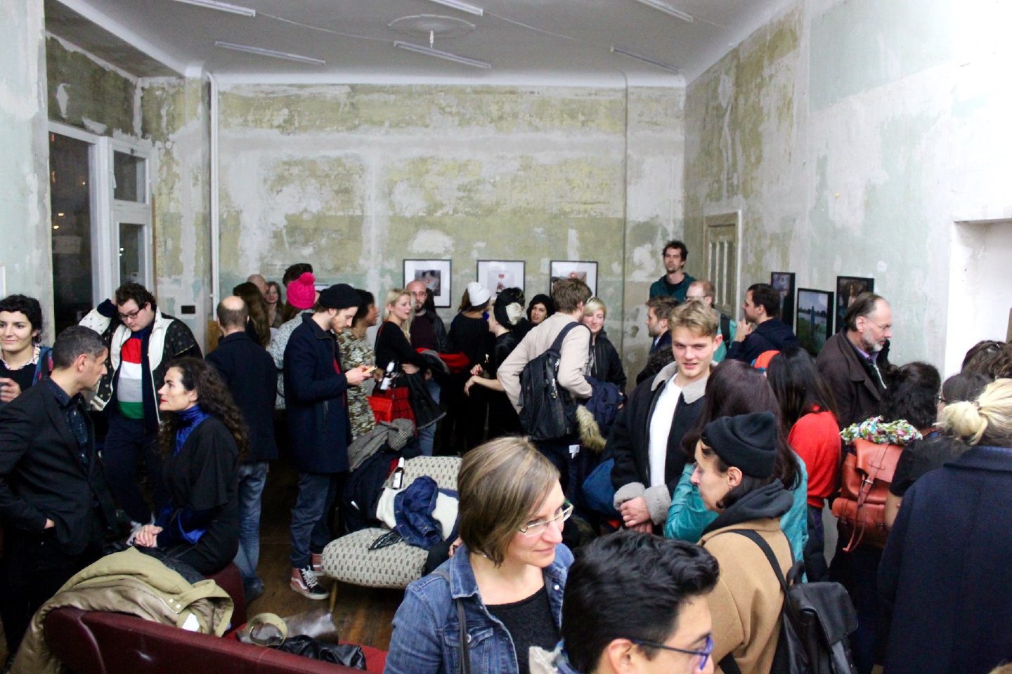 A crowded opening in a room with weathered green walls, framed photographs hung along the far side.