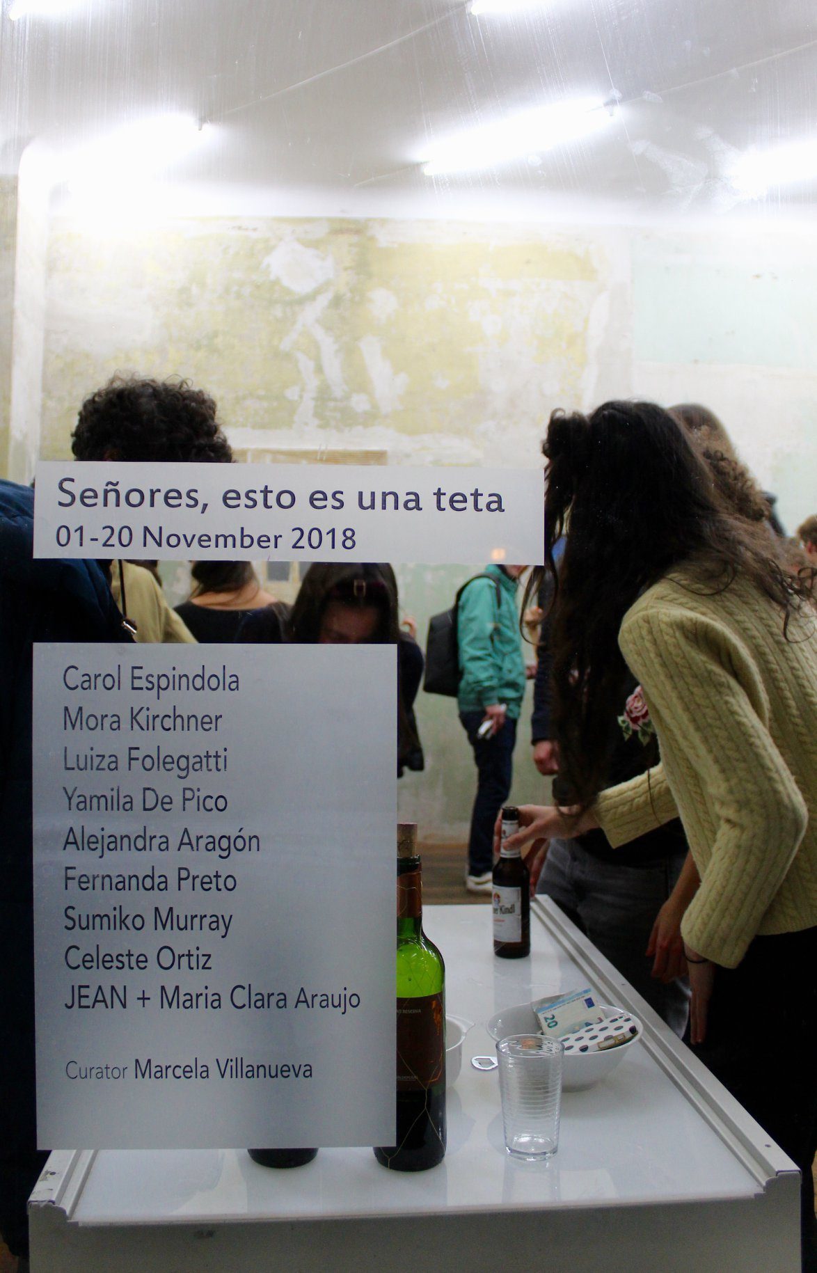 A printed wall panel reading “Señores, esto es una teta, 01–20 November 2018”, listing Carol Espindola, Mora Kirchner, Luiza Folegatti, Yamila De Pico, Alejandra Aragón, Fernanda Preto, Sumiko Murray, Celeste Ortiz and JEAN + Maria Clara Araujo, with Marcela Villanueva as curator.