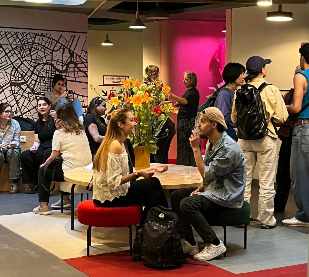 Visitors gathered in a hotel lobby with a large map mural; the pink-lit micro-gallery glows at the back of the room.